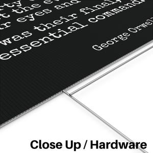 May include: Black sign with white text quoting George Orwell. The sign has a corrugated texture and is supported by a metal frame. The text reads "...was their final essential command."