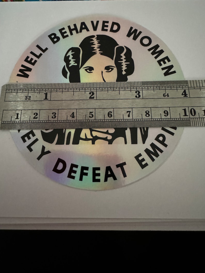 May include: A silver holographic sticker with black text that reads "Well Behaved Women Rarely Defeat The Empire". The sticker features a black and white illustration of Princess Leia from Star Wars.
