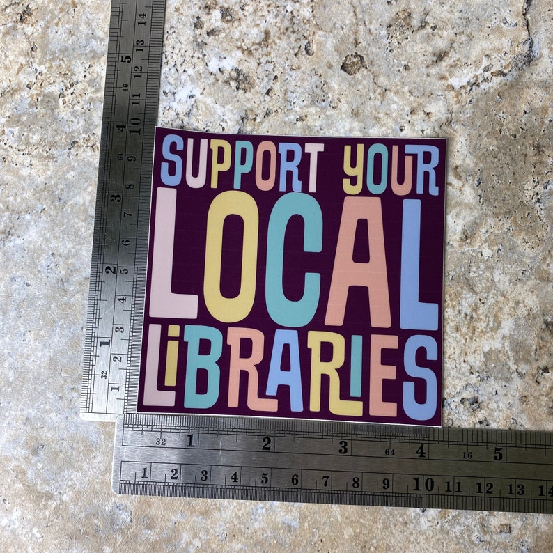 May include: A sticker with the text "SUPPORT YOUR LOCAL LIBRARIES" in colorful letters on a dark purple background.