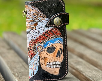 May include: A black leather wallet with a hand-tooled design of a skull wearing a Native American headdress. The headdress is decorated with feathers in shades of white, red, and blue.