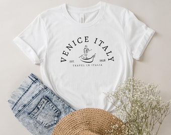 May include: White t-shirt with a black graphic design that says "Venice Italy Est. 1928 Travel in Italia" with a drawing of a person in a gondola.
