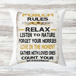 May include: White throw pillow with a black and gold design. The pillow features the text "Porch Rules" with a sunflower graphic and the text "Relax, Listen to Nature, Forget Your Worries, Live in the Moment, Gather with Loved Ones, Count Your Blessings".