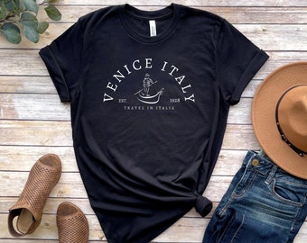 May include: Black t-shirt with a white graphic design that says "Venice Italy Est. 1928 Travel in Italia" with a drawing of a person in a gondola.