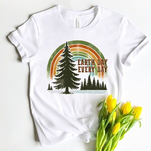 May include: White t-shirt with a retro-style graphic of a pine tree and rainbow with the text "Earth Day Every Day".