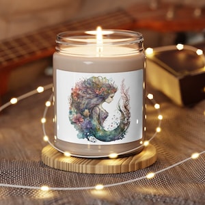 May include: A brown glass candle with a white label featuring a watercolor illustration of a woman with flowing hair and a floral crown. The woman is surrounded by flowers and water, creating a whimsical and ethereal design.