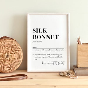 Puede incluir: Una impresi&oacute;n enmarcada con la palabra "SILK BONNET" en negrita en negro, seguida de la pronunciaci&oacute;n "/silk b&auml;nət/" y la definici&oacute;n: "sustantivo 1. protector, amigo fiel y guardi&aacute;n de tu cabello. 11. incluso cuando se desliza y desaparece misteriosamente por la noche, siempre te quedar&aacute;s a su lado. cuidado del cabello de primera"