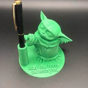 May include: Green 3D printed pen holder shaped like a character from Star Wars, with the text "May the Force be with you" on the base.