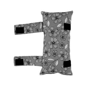 May include: Gray floral pillow with black straps. The pillow has a white floral pattern on a gray background.