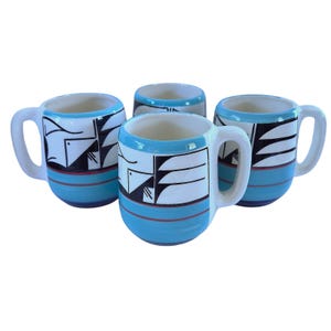 May include: A set of four ceramic mugs featuring a bright blue base, a white interior, and a black and white geometric graphic pattern around the middle. Each mug has a sturdy handle and a smooth, glossy finish with thin red horizontal lines.