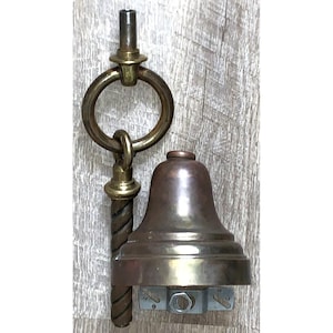 May include: A brass bell fixture featuring a smooth, flared bell shape attached to a vertical, twisted metal rod. A circular ring sits above the bell, connected to a threaded top post. A silver-toned metal mounting bracket is visible at the base.