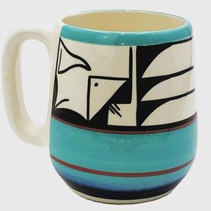 May include: A ceramic mug with a cream-colored handle and interior. The mug features a turquoise band and a design of black and white geometric shapes. A thin red stripe accents the turquoise band.