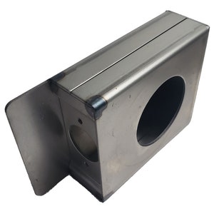 May include: A rectangular, silver-colored metal box with a large circular opening and a smaller hole. The box has a hinged side and visible weld marks at the corners, suggesting a handcrafted or industrial design.