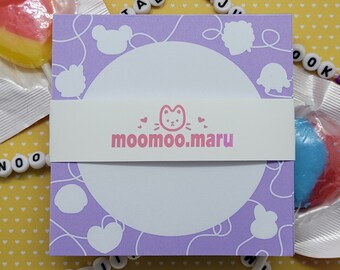 May include: Purple notepad with a white circle in the centre and a pink cat logo that says "moo moo.maru". The notepad has a white border and is decorated with white cartoon animal silhouettes.