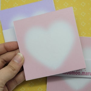 May include: A pink card with a white heart shape in the center. The card has a subtle ombre effect, fading from a darker pink at the edges to a lighter pink in the center. The card is blank and ready for writing.