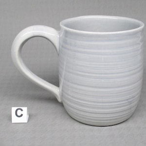 May include: A white ceramic mug with a light gray striped pattern. The mug has a rounded handle.