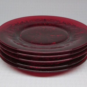 May include: A stack of four ruby red glass plates. The plates are round with a slightly raised rim and a subtle decorative pattern. The plates are stacked on top of each other, showcasing their rich color and design.