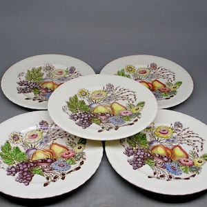 May include: Set of five white ceramic dinner plates with a floral and fruit design. The plates feature a central motif of peaches, grapes, and flowers in shades of pink, purple, green, and brown.