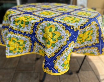 May include: A blue and white tablecloth with a lemon and flower pattern. The tablecloth has a yellow border and is made of a cotton fabric.