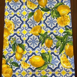 May include: A white fabric kitchen towel with a blue and yellow geometric pattern featuring lemons and leaves.