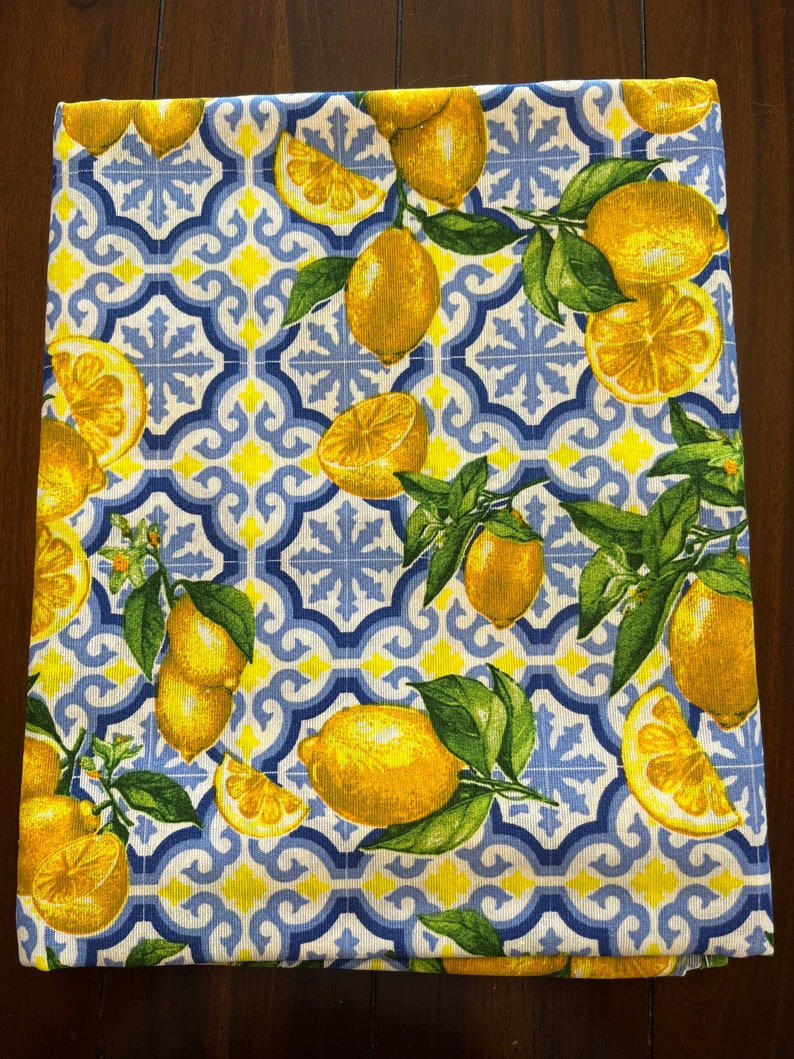 May include: A white fabric kitchen towel with a blue and yellow geometric pattern featuring lemons and leaves.