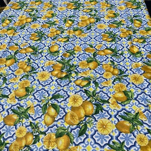 May include: A blue and white tablecloth with a lemon pattern. The tablecloth features a repeating pattern of lemons, leaves, and a blue and white tile design.