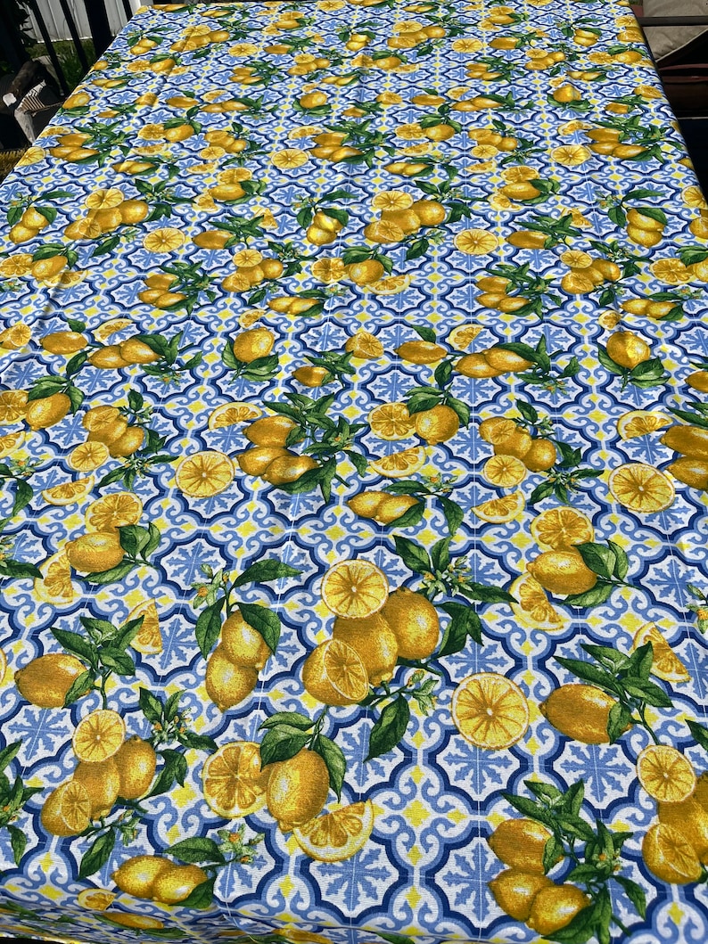 May include: A blue and white tablecloth with a lemon pattern. The tablecloth features a repeating pattern of lemons, leaves, and a blue and white tile design.