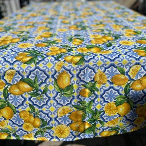May include: A white tablecloth with a blue and yellow lemon pattern. The tablecloth features a repeating pattern of lemons, leaves, and blue and yellow tiles.