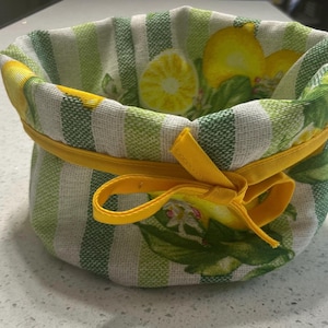 May include: A green and white striped fabric basket with a yellow ribbon and lemon print. The basket is perfect for storing small items.