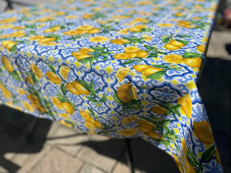 May include: A blue and white tablecloth with a lemon pattern. The tablecloth has a repeating pattern of lemons, leaves, and blue and white tiles.