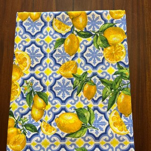 May include: A white kitchen towel with a blue and yellow pattern of lemons and stylized tiles.