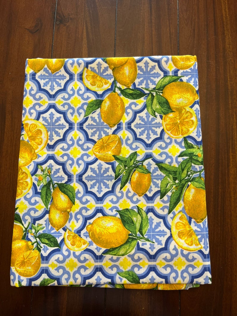 May include: A white kitchen towel with a blue and yellow pattern of lemons and stylized tiles.