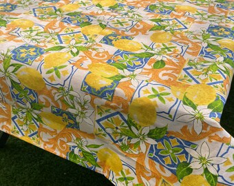May include: A white tablecloth with a lemon and floral pattern. The tablecloth features a repeating design of lemons, flowers, and blue and orange tiles.