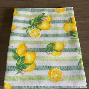 May include: White kitchen towel with green stripes and a lemon print. The lemons are yellow with green leaves.