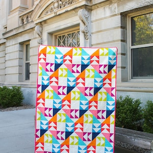 May include: A colorful quilt with a geometric pattern of triangles and circles in shades of pink, orange, blue, green, and yellow. The quilt is made of cotton fabric and is quilted with a white thread.