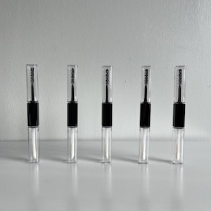 Puede incluir: Cinco aplicadores cosméticos dobles transparentes con tapas y mangos negros están dispuestos en fila. Cada aplicador tiene un cepillo en un extremo y una varilla en el otro. Los aplicadores están sobre una superficie blanca contra un fondo blanco.