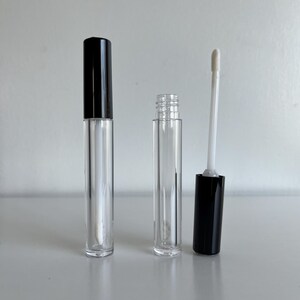 May include: Two clear plastic tubes with black caps and a white applicator wand. The tubes are empty and ready to be filled with lip gloss or other liquids.