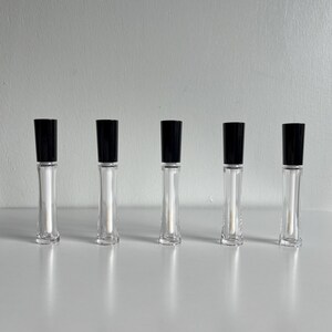 May include: Five clear glass bottles with black caps. The bottles are filled with a clear liquid and have a rounded bottom.