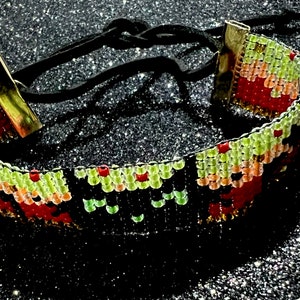 May include: A colorful beaded choker necklace with a black cord and gold metal clasps. The beads are arranged in a geometric pattern with red, orange, yellow, green, and black colors.