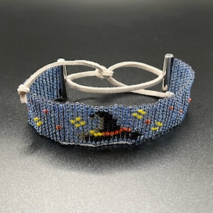 May include: A blue beaded bracelet with a witch and hat design. The bracelet has a leather strap closure.