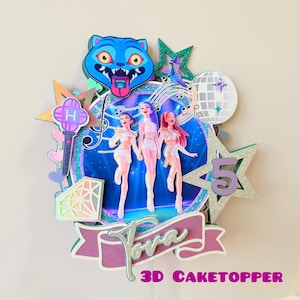 May include: A colorful 3D cake topper featuring three stylized figures in white outfits, a blue cat-like character, and a disco ball. The design includes stars, musical notes, and the number 5. The text "Tora" and "3D CAKETOPPER" are also visible.