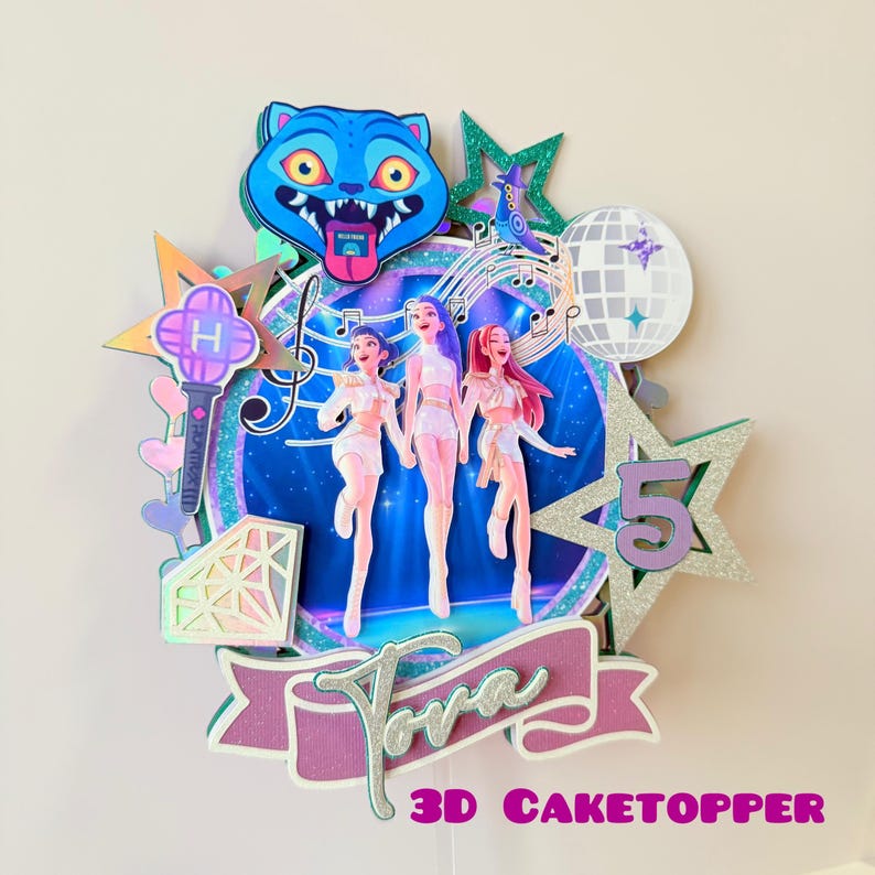 May include: A colorful 3D cake topper featuring three stylized figures in white outfits, a blue cat-like character, and a disco ball. The design includes stars, musical notes, and the number 5. The text "Tora" and "3D CAKETOPPER" are also visible.