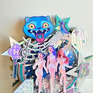 May include: A layered birthday cake topper featuring three stylized figures, musical notes, and a blue cat face. The design includes a disco ball, a star with the number 13, and a holographic background with glitter accents.