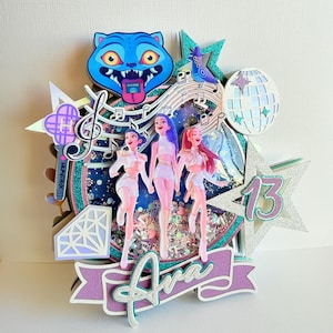 May include: A layered cake topper featuring three stylized figures, musical notes, and a disco ball. The topper includes a blue cat face, a star with the number 13, and a banner that says "Ava". The color palette includes shades of blue, pink, and silver.