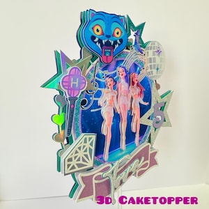 May include: A multi-layered cake topper featuring a blue cartoon cat head, three stylized figures, musical notes, stars, and a disco ball. The topper includes the text "3D CAKETOPPER" and a banner that says "Three".