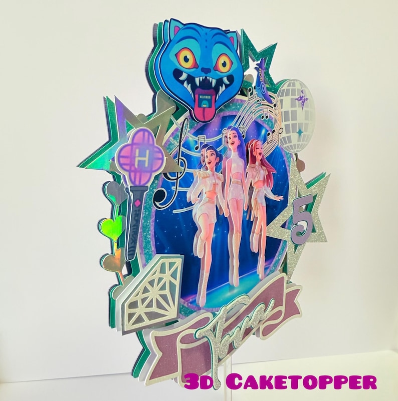 May include: A multi-layered cake topper featuring a blue cartoon cat head, three stylized figures, musical notes, stars, and a disco ball. The topper includes the text "3D CAKETOPPER" and a banner that says "Three".
