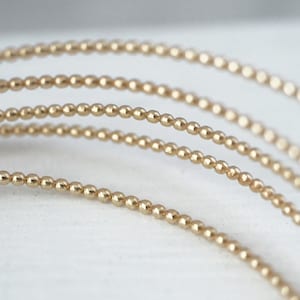 以下が含まれることがあります： 金色のビーズワイヤーのクローズアップ。ビーズの質感とディテールがわかります。