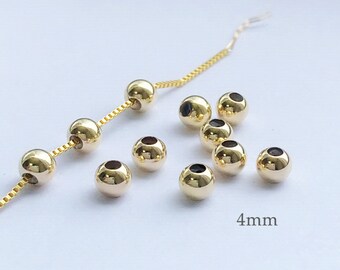 May include: A close-up of ten gold-colored metal beads, each measuring 4 mm in diameter. The beads are arranged in a scattered pattern on a white surface.