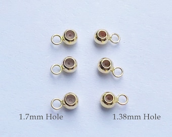 May include: Six gold-colored metal bead caps with a loop on one side. Three of the bead caps have a 1.7mm hole and three have a 1.38mm hole.