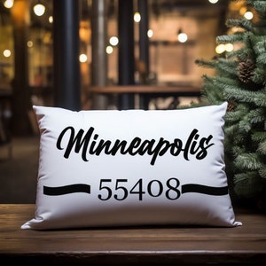 May include: White pillow with black text that reads "Minneapolis - 55408". The pillow is on a wooden surface with a Christmas tree in the background.