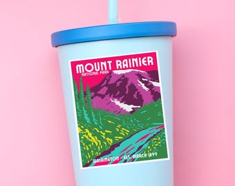May include: A light blue tumbler with a blue lid and a light blue straw featuring a rectangular sticker of Mount Rainier National Park. The sticker displays a purple mountain, green trees, and a blue path with the text Mount Rainier National Park Washington Est. March 1899.